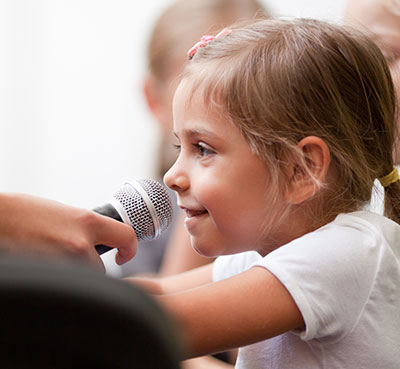 Smiling five year old girl speaks into handheld microphone